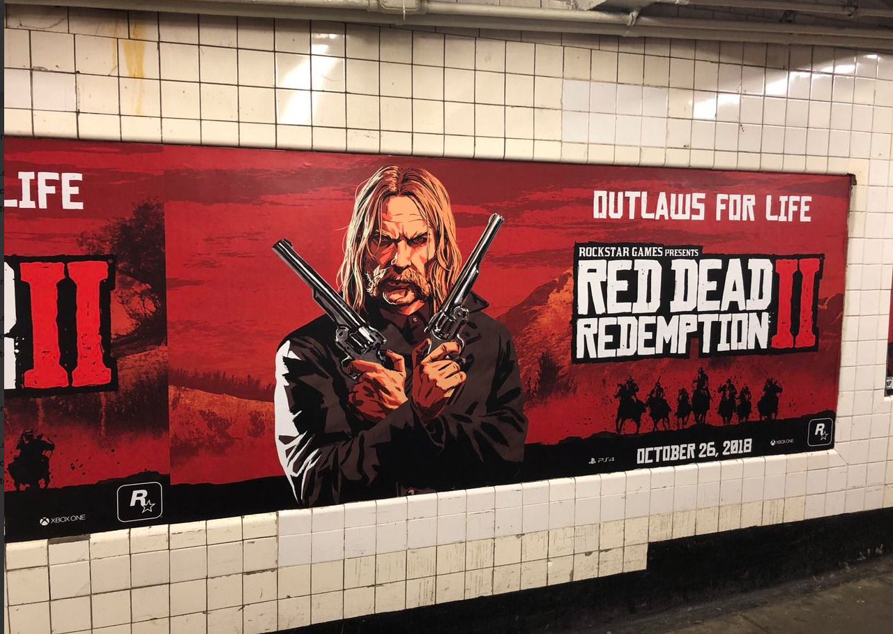 A red Red Dead Redemption 2 poster reading “Outlaws for Life”, showing a long-haired gunslinger holding two revolvers, dated October 26, 2018, on a NYC subway station wall.